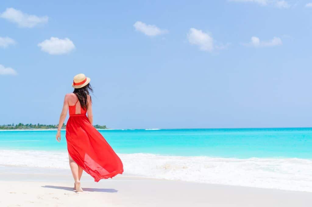 jeune femme portant une robe fluide à la plage et un chapeau pour se protéger du soleil
