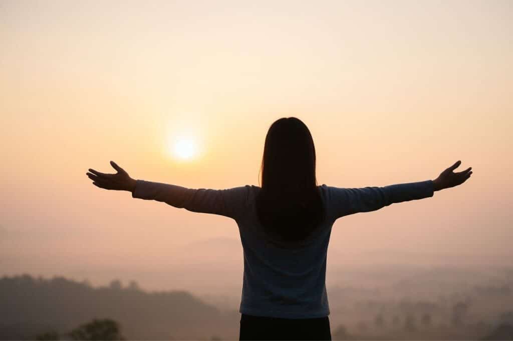 silhouette d'une femme bras ouverts face au lever du soleil, symbolisant la sortie du syndrome de la vie vide et le renouveau intérieur