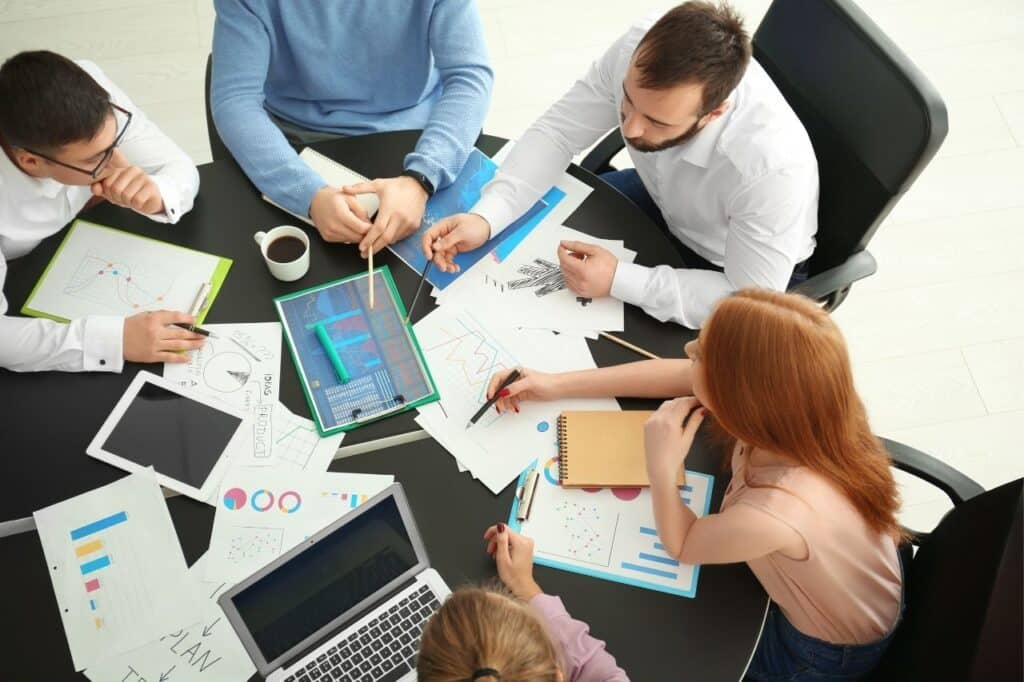 Équipe digitale réunie autour d’une table, avec un développeur, un spécialiste data, un expert cybersécurité et une responsable marketing collaborant sur un projet commun.